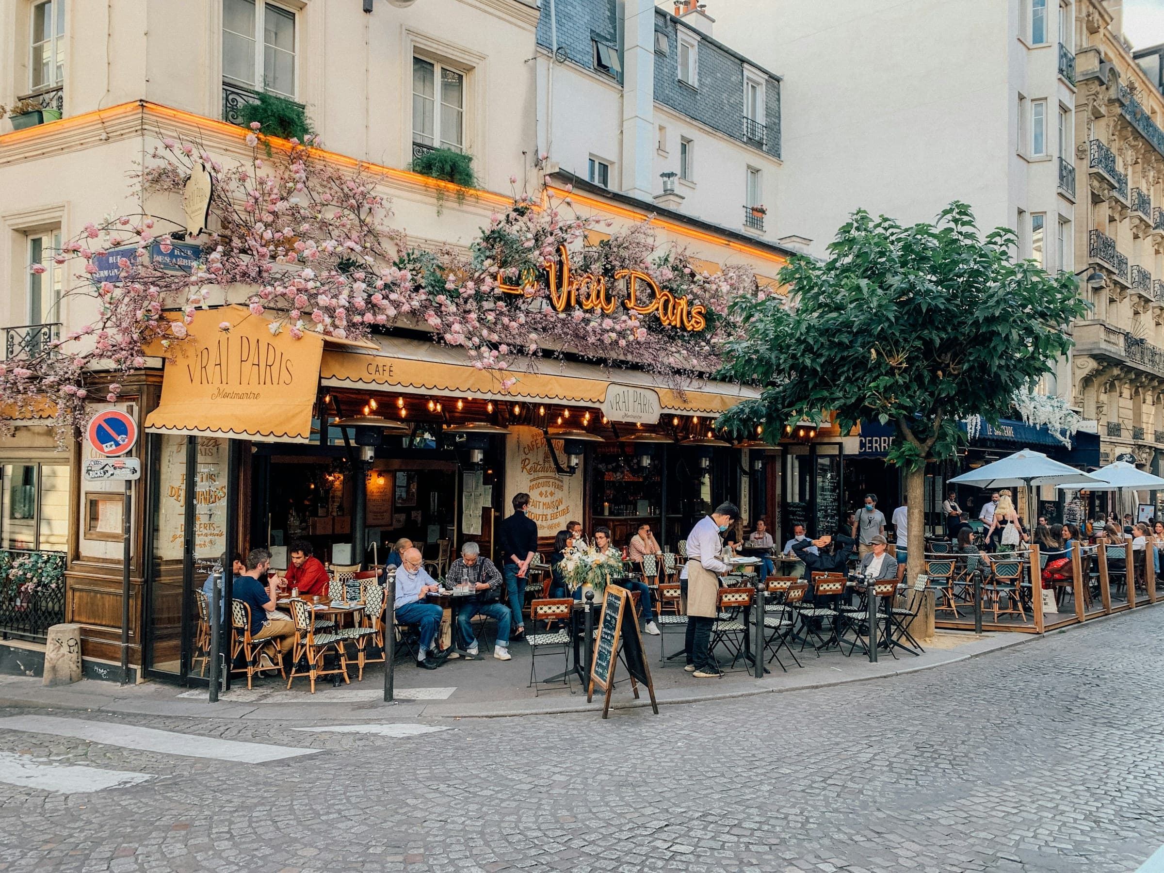 A Parisian café terrace on a street corner, with flowers above the awning